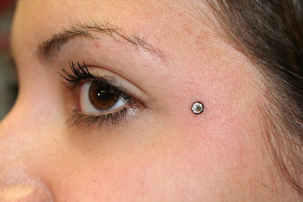 Microdermal Piercing Implantat am Auge gestpchen mit schwarzer Disc und Glitzerstein